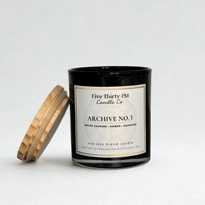 Archive No. 3 Becoming Still candle by Five Thirty PM Candle Co® in a black glass jar with a wooden lid and white jasmine, amber, and oakmoss fragrance notes.