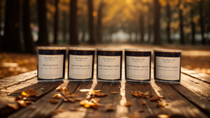 Coming Home candle collection featuring The Way Back, Like It Used To Be, Make Yourself Home, Right Where I Belong, and Just What I Needed candles in black jars with bamboo lids, displayed in a warm fall woodland setting by Five Thirty PM Candle Co®.