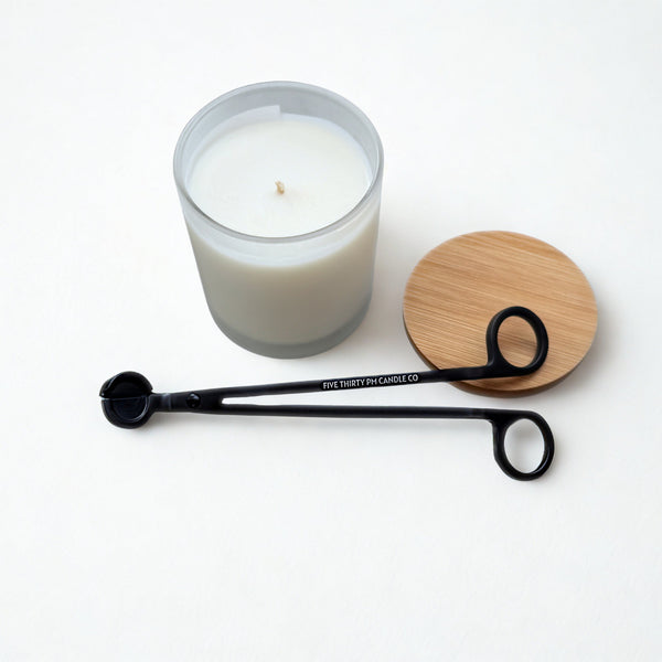 Matte black stainless steel wick trimmer engraved with Five Thirty PM Candle Co® displayed beside a candle and bamboo lid on a white background.