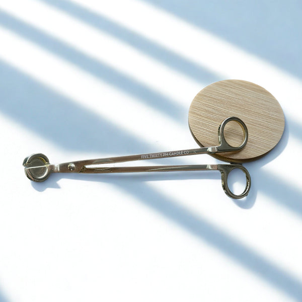 Stainless steel candle wick trimmer with engraved Five Thirty PM Candle Co® logo displayed with a bamboo candle lid for candle care.