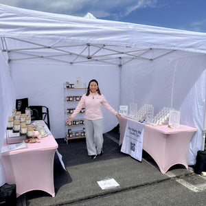 Ivy, founder and candle maker of Five Thirty PM Candle Co®, standing inside her outdoor market booth with displays of handcrafted candles, wax melts, and candle accessories at Loudoun Spring Market.