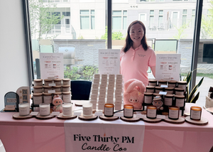 Ivy, founder and candle maker of Five Thirty PM Candle Co®, standing behind a market display featuring Glow Up and Archive of Life candles and wax melts at M. Flat Pop & Shop.