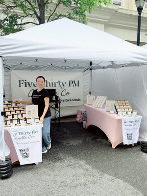 Ivy, founder and candle maker of Five Thirty PM Candle Co®, standing inside her outdoor market booth with displays of handcrafted candles, wax melts, and candle accessories at Anchors & Artisans August market hosted by the Makers of Maryland