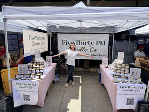 Ivy, founder and candle maker of Five Thirty PM Candle Co®, standing inside her outdoor market booth with displays of handcrafted candles, wax melts, and candle accessories at The Maker's Valley x Boordy Vineyards Summer Festival.