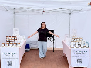 Ivy, founder and candle maker of Five Thirty PM Candle Co®, standing inside her outdoor market booth with displays of handcrafted candles, wax melts, and candle accessories at Frederick Spring Festival.
