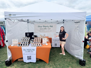 Ivy, founder and candle maker of Five Thirty PM Candle Co®, standing inside her outdoor market booth with displays of handcrafted candles, wax melts, and candle accessories at Twinbrook Quarter Makers Market hosted by the Maker's Valley