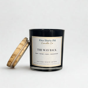 The Way Back candle by Five Thirty PM Candle Co® in a black glass jar with a wooden lid and pine, thyme, sage, and cedarwood fragrance notes.